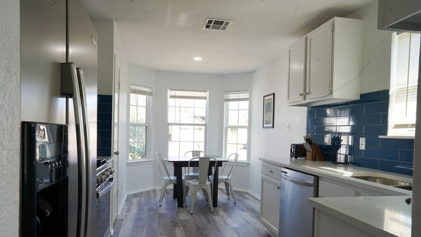 Eine Küche mit weißen Schränken, einem schwarzen Kühlschrank, einer blauen Fliesenrückwand und einem Essbereich mit Tisch und Stühlen.
