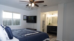 Ein Schlafzimmer mit Bett, Deckenventilator, Fernseher und angrenzendem Badezimmer.