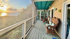 Un balcon abrité, doté de meubles en osier et offrant une vue sur l’océan au coucher du soleil.