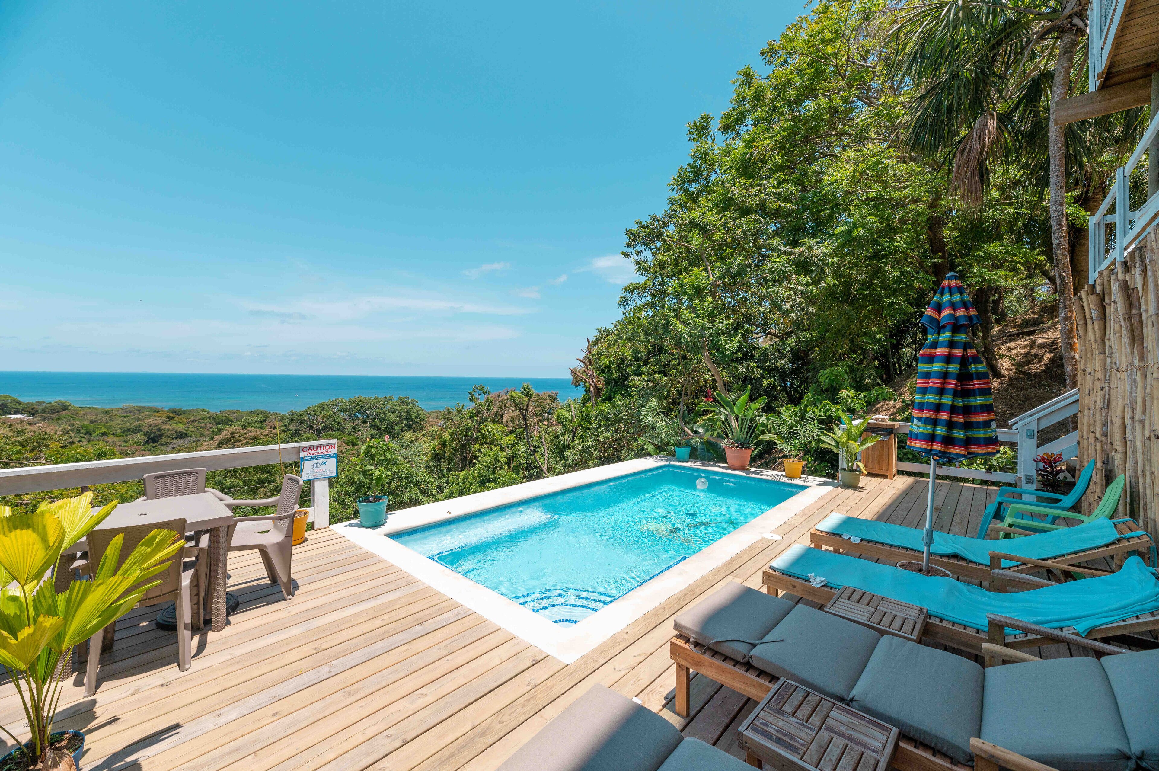 Eine Holzterrasse mit Schwimmbad, Liegestühlen und Blick aufs Meer.