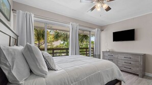 A bedroom with a bed, a ceiling fan, a TV, and a balcony with curtains. - 2 bedroom, walk to the Beach! Sleeps 6, outdoor games and yard space! (Fort Walton Beach)