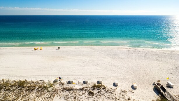 A beach with clear turquoise water, a sandy shore, and a few umbrellas. - 2 bedroom, walk to the Beach! Sleeps 6, outdoor games and yard space! (Fort Walton Beach)