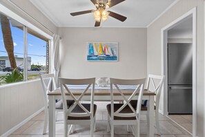 A dining area with a table and chairs, a ceiling fan, a refrigerator, and a window with a view of the outside. - 2 bedroom, walk to the Beach! Sleeps 6, outdoor games and yard space! (Fort Walton Beach)