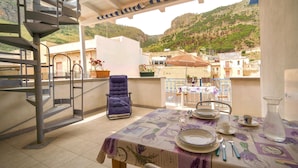 Ein Balkon mit Esstisch, Stuhl, Topfpflanze und Blick auf eine Hügelkette.