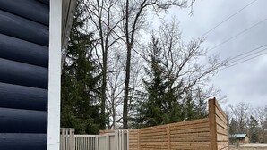 En bostadsfastighet med en gång av betong som leder till en träveranda, omgiven av ett trästaket och träd.