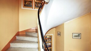 Eine Treppe mit Handlauf, einem Heizkörper und einem Regal mit Gegenständen an der Wand.