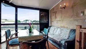 Ein Zimmer mit Glastisch, Stühlen, einer Couch und Blick auf Gebäude durch große Fenster.