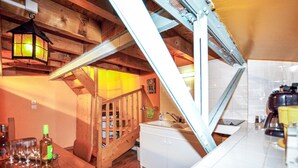 Eine rustikale Küche mit Holzbalken, einer Holztreppe, einem weißen Spülbecken und einem Essbereich mit Tisch und Stühlen.