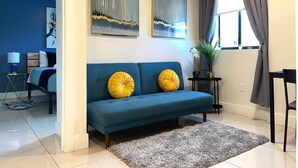 Un salon moderne avec un canapé bleu, deux coussins jaunes, un tapis gris et des œuvres d’art abstraites accrochées au mur.