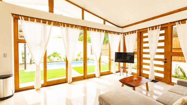 A spacious living room with a large window, a flat-screen TV, and a sofa. - Villa Akari - Modern and Sophisticated Villa close to the Beach (Puntarenas Province)