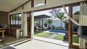 A spacious living area with a large sliding glass door leading to a backyard with a pool and outdoor furniture. - Villa Akari - Modern and Sophisticated Villa close to the Beach (Puntarenas Province)