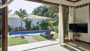 A room with a large sliding glass door leading to a pool area, a flat-screen TV, and a small table. - Villa Akari - Modern and Sophisticated Villa close to the Beach (Puntarenas Province)