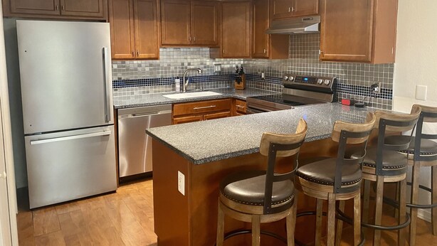 A modern kitchen with wooden cabinets, a stainless steel refrigerator, a built-in oven, and a granite countertop.