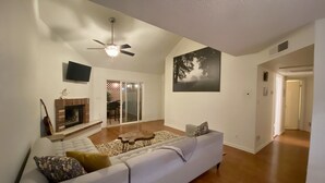 A living room with a sectional sofa, a fireplace, a ceiling fan, and a large painting on the wall.