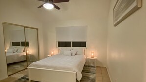 A bedroom with a bed, a ceiling fan, a large mirror, and bedside lamps.