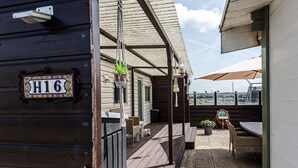 Een houten gebouw met een veranda, een bordje met de tekst 'H16', buitenterras met parasols en potplanten.