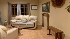 Una sala de estar con un sofá beige, un banco de madera, una chimenea y un cuadro en la pared.