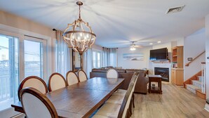 A spacious living room with a large wooden dining table, comfortable seating, a fireplace, and a staircase leading to an upper level. - 5BR Steps to Beach & Boardwalk! Beach tags & 3 parking spaces included! (Ocean City)