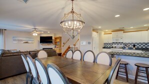 A spacious living room with a large wooden dining table, comfortable seating, a chandelier, and a kitchen area with modern appliances. - 5BR Steps to Beach & Boardwalk! Beach tags & 3 parking spaces included! (Ocean City)