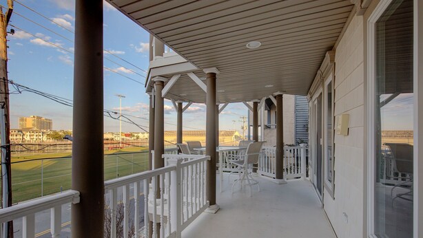 A covered porch with white railings, outdoor seating, and a view of a sports field. - 5BR Steps to Beach & Boardwalk! Beach tags & 3 parking spaces included! (Ocean City)