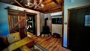 Interno di una baita rustica con soffitto in legno, un lampadario, un camino e un televisore.