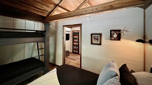 Una camera rustica con un letto a castello, un soffitto in legno e un corridoio che conduce al bagno.