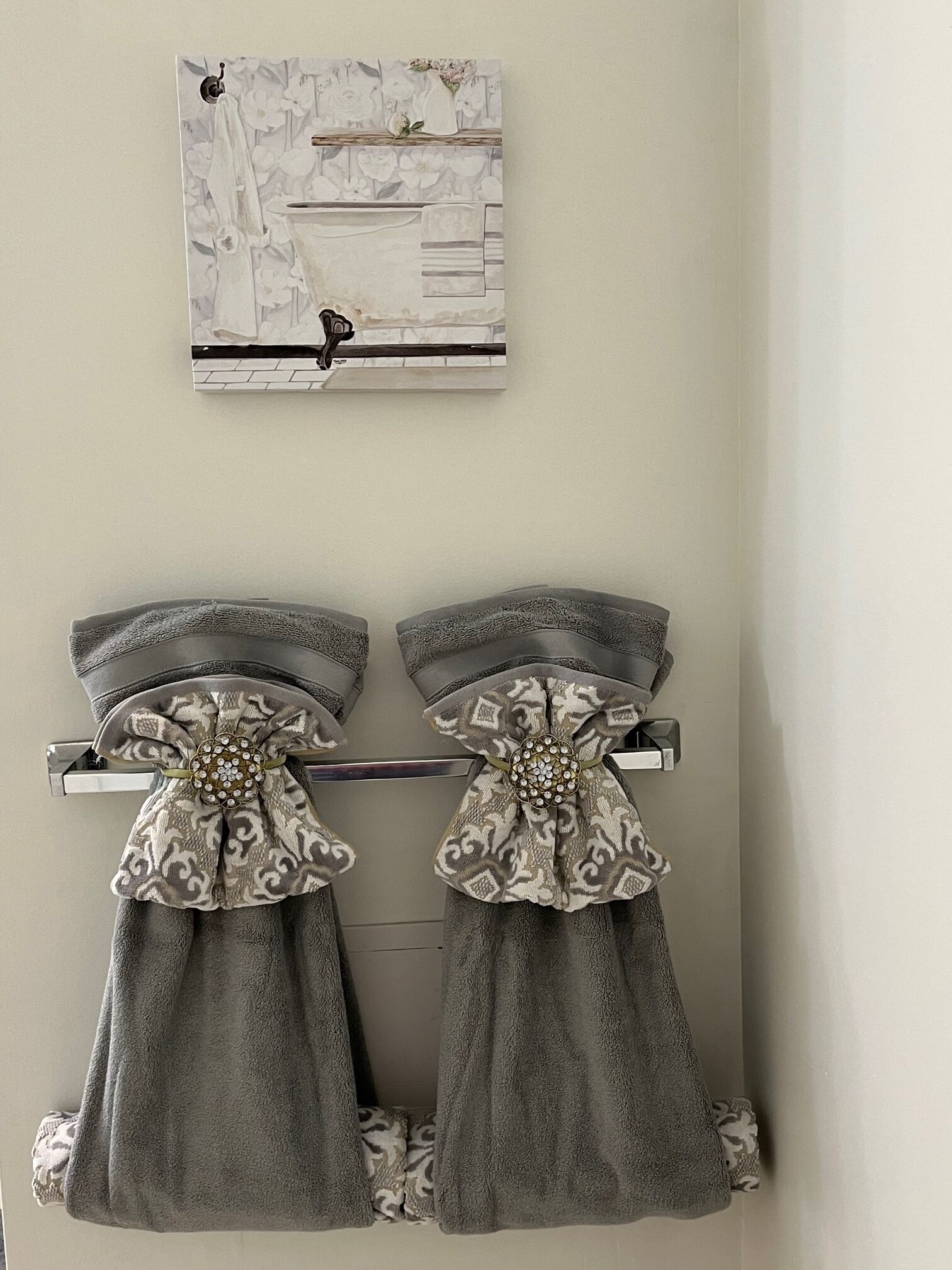 Un baño con dos toalleros que sostienen toallas grises adornadas con lazos decorativos. Sobre los toalleros, hay una obra de arte enmarcada con un estampado floral.
