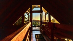 A wooden interior leading to a balcony with a table and chairs, a view of the outdoors, and a door with triangular glass panels. - Spacious Retreat~ Hot Tub~ Stunning Views~ Game Room (Mineral Bluff)