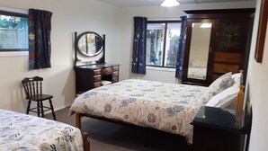 A bedroom with a bed, a dresser, a chair, a desk, a mirror, and a window with curtains. - Spacious Garden Cottage w/ woodburner (Waitara)