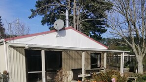 A single-story house with a red roof, a satellite dish, and a garden with various plants and flowers. - Spacious Garden Cottage w/ woodburner (Waitara)