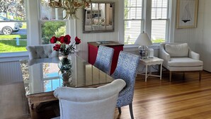 A dining area with a glass table, two chairs, a vase with red flowers, a chandelier, and a red cabinet. - The beach is waiting. (East Lyme)