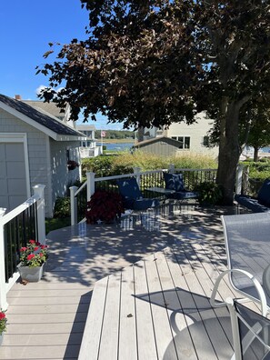 A wooden deck with outdoor furniture, a white fence, and a tree providing shade. - The beach is waiting. (East Lyme)