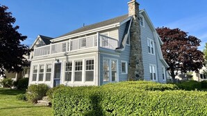A large, two-story house with a stone chimney, multiple windows, and a well-maintained lawn. - The beach is waiting. (East Lyme)