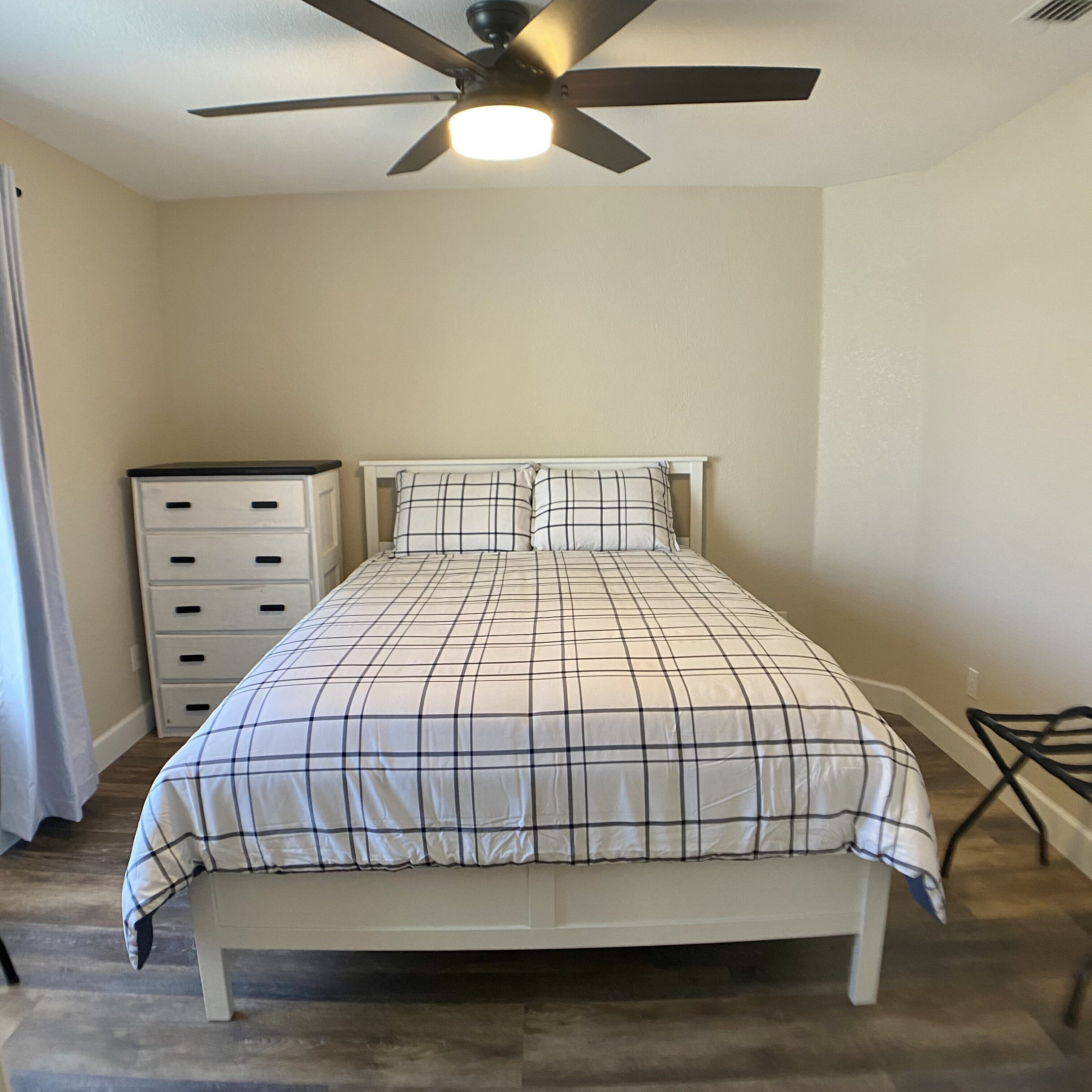 A bedroom with a bed, a ceiling fan, a dresser, and a chair.