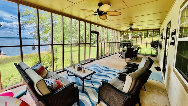 A covered patio with wicker furniture, a ceiling fan, and a view of a lake.