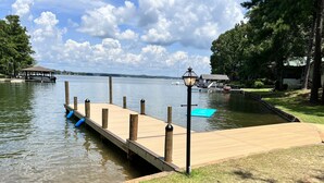 A wooden dock extending into a calm lake, with a lamp post and a gazebo in the background.