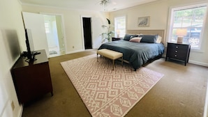 A bedroom with a bed, a bench, a dresser, a nightstand, a ceiling fan, and a window.
