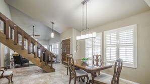 Un coin repas avec une table et des chaises en bois, un escalier et un ventilateur de plafond.