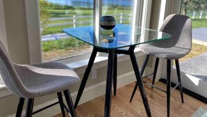 A modern room with a glass table and two grey chairs, large windows with a view of a lake and greenery. - Chesapeake Paradise House-Stunning 6+br4ba Wtrfrnt (Deale)