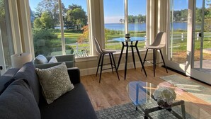 A living room with a sofa, two chairs, a glass coffee table, and large windows overlooking a lake. - Chesapeake Paradise House-Stunning 6+br4ba Wtrfrnt (Deale)