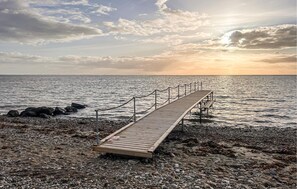 Une jetée en bois s’étendant dans des eaux calmes, bordée d’une côte rocheuse.