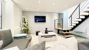 Un salon moderne avec un canapé, une table basse, un téléviseur et un escalier.