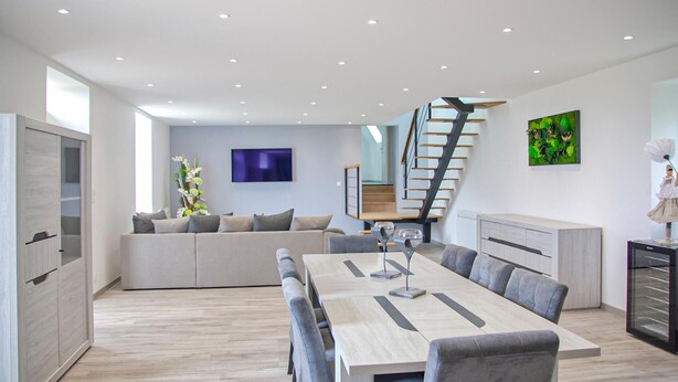 Un espace de vie moderne comprenant un coin repas, un ensemble de canapés, un escalier et un téléviseur à écran plat.