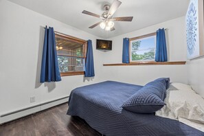 Ein Schlafzimmer mit einem Bett, einem Deckenventilator und zwei fensterbepflanzten Fenstern.