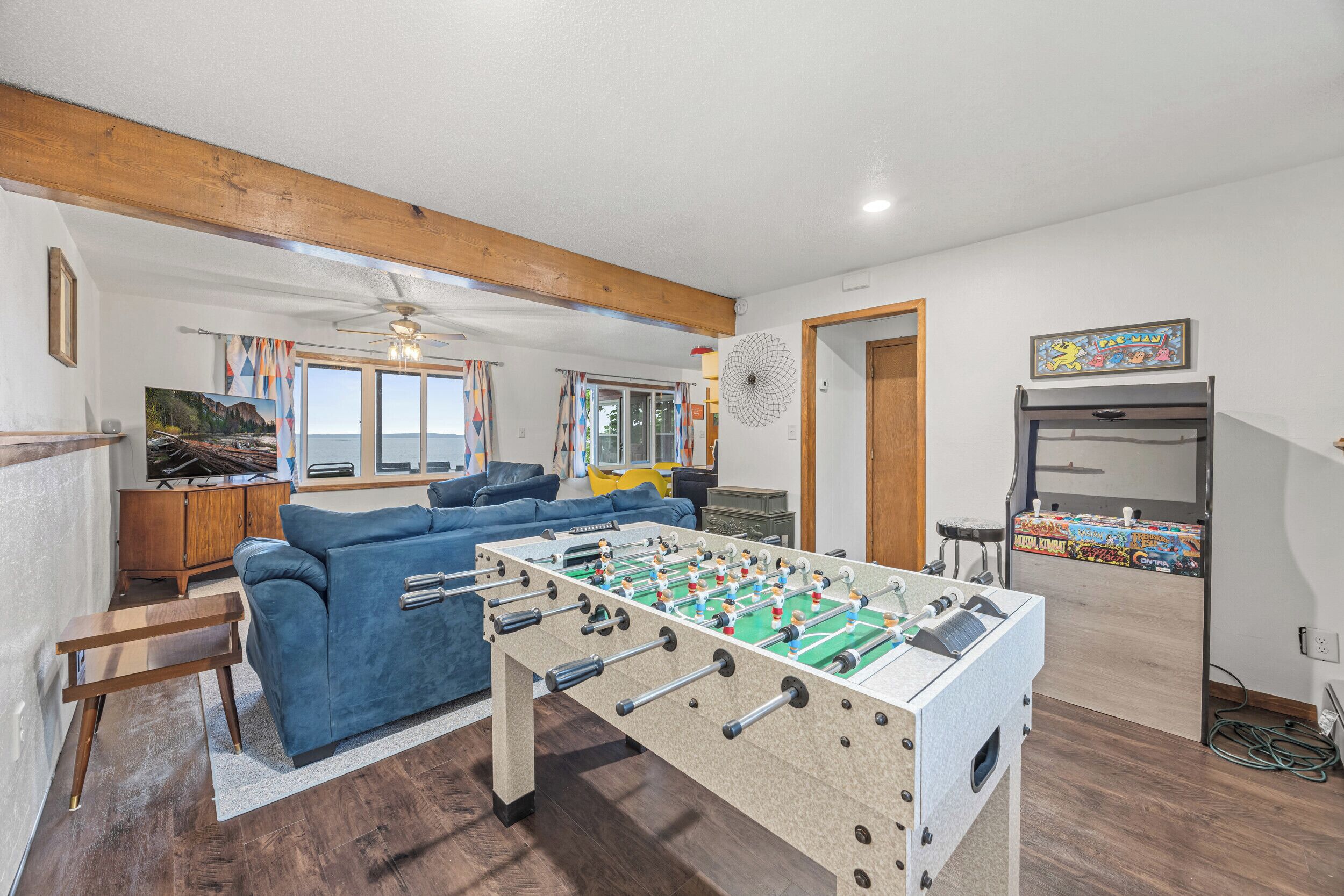 Ein Raum mit Tischfußball, einem blauen Sofa, Holzboden und Deckenventilator.