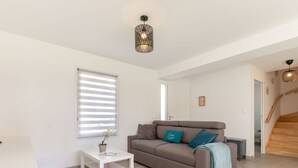 A living room with a grey sofa, a white coffee table, and a window with blinds. - Beautiful  villa for 6 people with WIFI, TV, terrace and pets allowed (Royan)