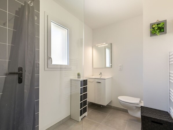 Un baño moderno con cabina de ducha de vidrio, un lavamanos blanco, un inodoro y una pequeña planta en maceta sobre el mueble.