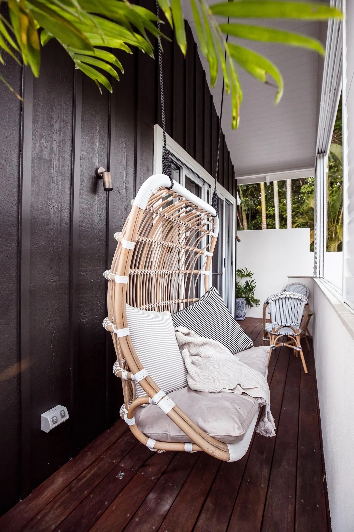 A wicker chair with cushions on a wooden deck, a small table, and a potted plant.