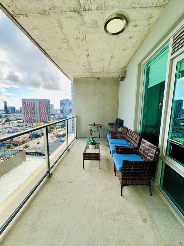 A balcony with a sofa, a small table with a plant, and a view of the cityscape.