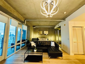 Un salon moderne doté d’une grande fenêtre, d’un canapé en cuir noir, d’une table basse en verre et d’un luminaire au plafond au design original.